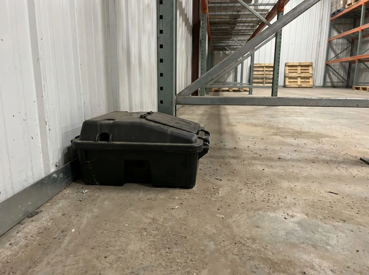 Tamper-resistant rodent bait station along a warehouse wall